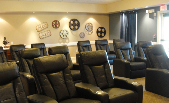 Stoney Brook assisted living, theater with dark leather theater seating, blue velvet drapes and movie reel artwork.