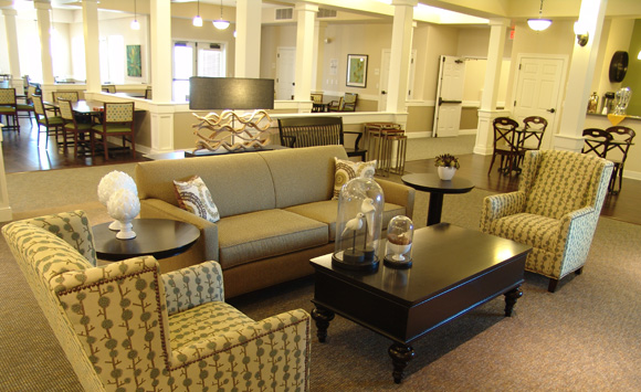 Formal living space in open plan of Stoney Brook senior living. Subtle palette creates a calming environment, wood accent lamp and nature inspired accessories.