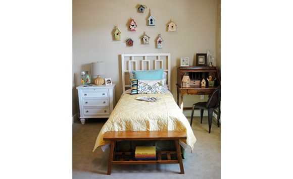 Bright yellow and white bedroom with vintage roll-top desk /chair and birdhouse collection above headboard.