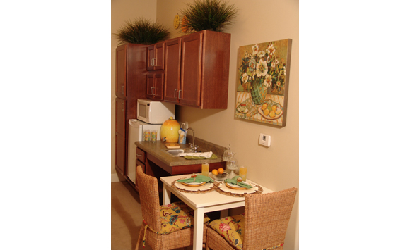 Assisted living studio kitchenette with white table, rattan chairs, and lemon accents.