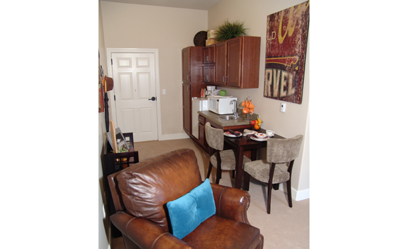 Assisted living studio living/kitchenette space with comfy brown leather chair and vintage artwork.