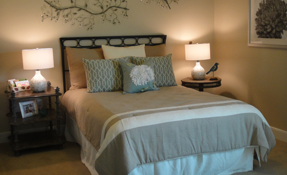 Taupe, white and blue custom bedding with capiz shell accent lamps. Vintage wood nightsands and decorative metal vine artwork.