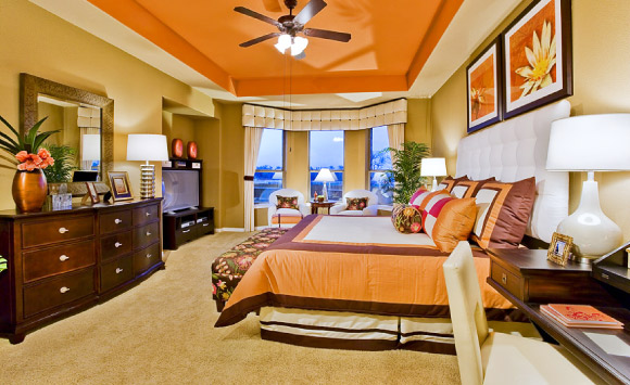 Bright orange accents from the tray ceiling to the custom bedding, ottoman and window treatments make this a unique master bedroom.